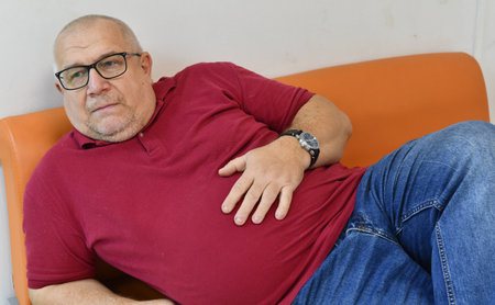 Senior man suffering from backache sitting on an orange armchair.の写真素材