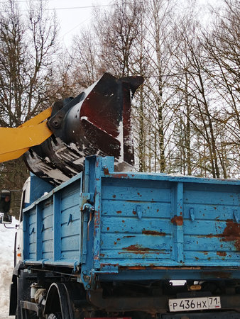 Dump truck unloads snow from the ground in the city.