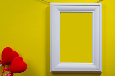 white frame hanging on a rope and two hearts on a yellow background, space for text