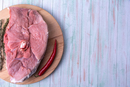 piece of pork meat on the bone, chilli, spices on a round wooden cutting board on top