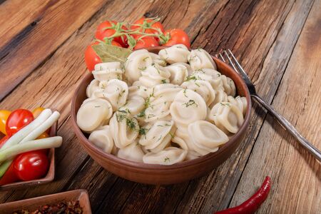 homemade dumplings with sour cream and dill on a wooden vintage table with fresh tomatoes, onions and spices in the style of rusticの写真素材