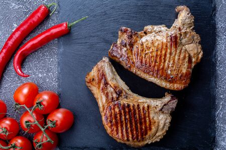 fried steaks on a slate stone with cherry tomatoes and chilli on a dark textured background look from aboveの写真素材