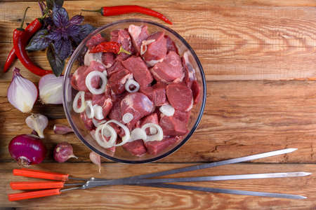 Cooking kebabs. Boneless lamb steak, cut into chunks, meat in a glass bowl. Onion, garlic, pepper, Basil and skewers for meat, on a wooden table. Sheep meat close-up. Lamb shish kebab. The view from the top.Rustic style.macroの写真素材