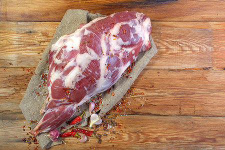 On a wooden table lies a raw leg of mutton on a bone. Sheep meat close-up.A fresh piece of mutton....