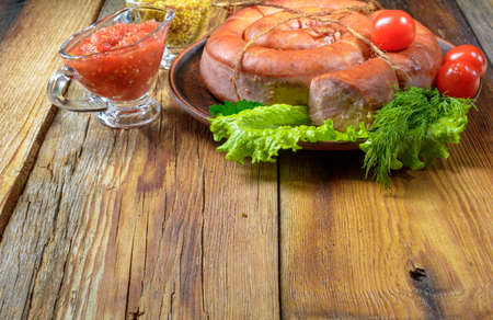 Smoked homemade pork sausage on a plate, a saucepan of mustard on an old wooden table.Country food.Selective focus.Horizontal view.の写真素材