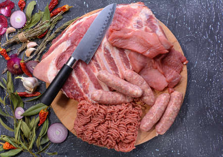 Raw meat products.Barbecue pork ribs, steaks, grilled sausages, minced meat, garnished with spices on a round wooden chopping board.Top view.Flat layout.Selective focus.の写真素材