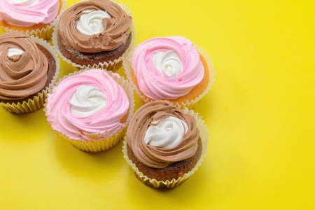 Chocolate and vanilla cupcakes with whipped raspberry and coffee cream on a yellow background. Selective focus.Horizontal viewの写真素材