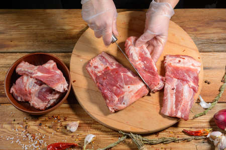 The chef uses his hands to slice pork ribs with a knife on a wooden cutting table. Selective focus. The concept of the cooking process.On a dark black background with a copy of the place for the text menu or recipe.の写真素材