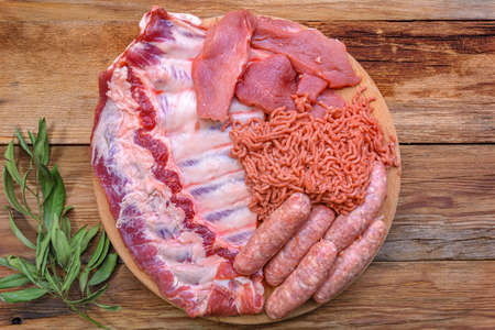cold cuts. raw pork ribs, minced meat, sausages, and carbonate on a round cutting board. Condiments for cooking meat dishes close-up. Selective focus, top viewの写真素材