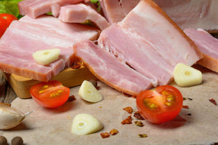 Smoked sliced pork belly, bacon, ham with herbs, tomatoes and black pepper on food paper. Wooden rustic background.Selective focus.Horizontal view.の写真素材