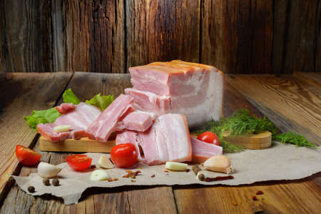 Smoked sliced pork belly, bacon, ham with herbs, tomatoes and black pepper on food paper. Wooden rustic background.Selective focus.Horizontal view.の写真素材