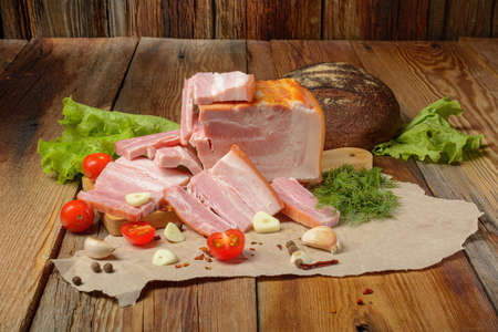 Smoked sliced pork belly, bacon, ham with herbs, tomatoes and black pepper on food paper. Wooden rustic background.Selective focus.Horizontal view.の写真素材