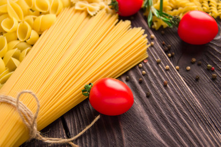 Variety of kinds and forms of dry macaroni with tomatoes and rosemary. Italian macaroni raw food or texture: pasta, spaghetti, pasta in the form of a spiral.の写真素材