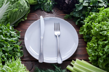 Green, juicy lettuce leaves in assortment with fork and knife on a white plate in the center view from aboveの写真素材