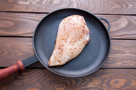 Raw fresh chicken fillet with herbs and spices for cooking, in a black frying pan made of iron, on a wooden table top viewの写真素材