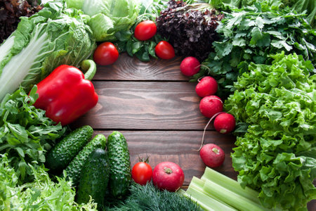 top view of green lettuce leaves, cucumber and red vegetables on wooden table with place for text centeredの写真素材