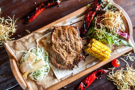 juicy grilled beef steak on a wooden board with corn, onion and pepper from the topの写真素材