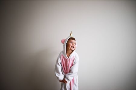 pretty girl wearing pink unicorn kigurumi and smiling, looking at window at white backgroundの写真素材