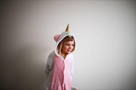 portrait of little todder girl standing next to a white wall, smiling, wearing unicorn kigurumiの写真素材