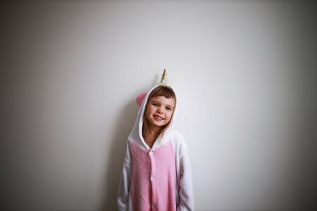 portrait of little todder girl standing next to a white wall wearing unicorn kigurumi and looking at camera half-body portraitの写真素材