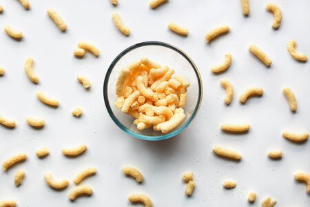 Sweet corn sticks in a glass bowl standing on white surface among other scattered around. Organization, collection concept.の写真素材