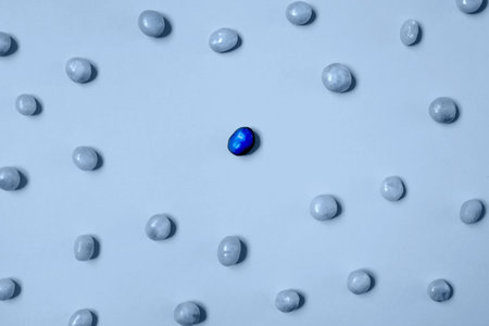 One dark blue candy bean among light blue ones on light blue background. Social distancing, stay...