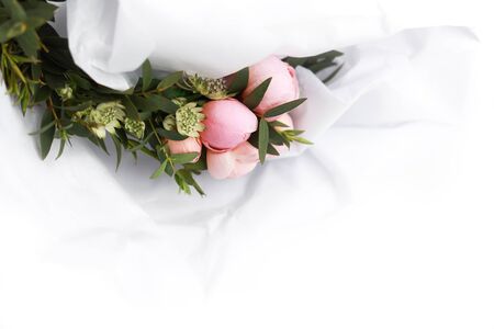 White floral background with pink roses among green leaves covered in white tissue paper.の写真素材