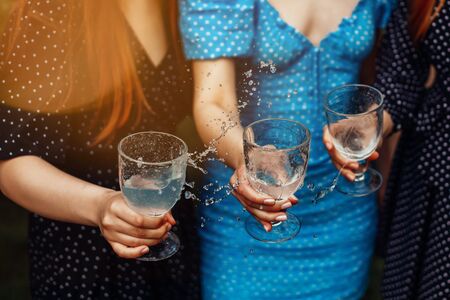 Three girls in polka dot dresses holding glasses with a drink. Cheering and making water splash.の写真素材