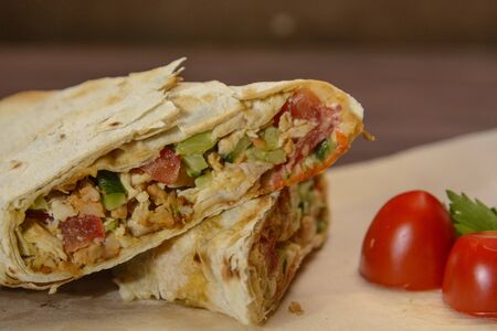 Sliced Shawarma with slices of tomato and herbs on the wood. Close up. Organic food.の写真素材