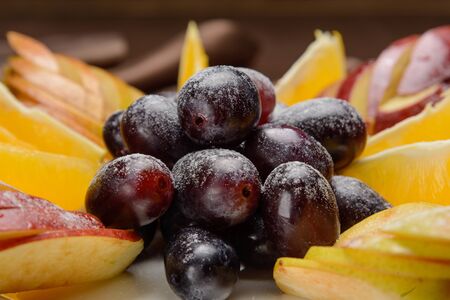 Fruit plate closeup. In the foreground are berries of black grapes.の写真素材