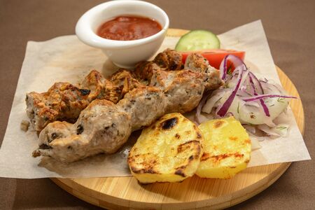 Kebab with fried potatoes, onion and vegetables on a wooden board.の写真素材