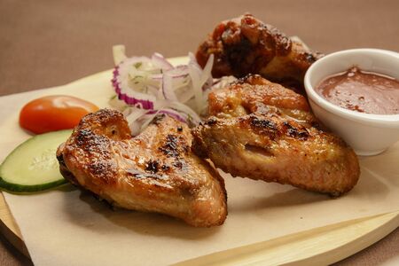 Fried chicken wings with onion rings and red sauce on a wooden board.の写真素材