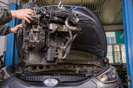 Car mechanic pulls out the engine from the car for repairの写真素材