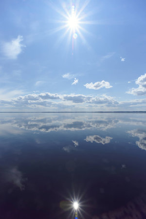 River view with clouds reflected in it, the sun in the frame and the reflection of the sun, Volga, Russiaの写真素材