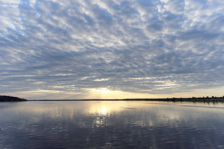 View of the golden sunset on the river with clouds and the Sun reflected in it, Volga, Russia.