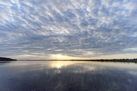 View of the golden sunset on the river with clouds and the Sun reflected in it, Volga, Russia.の写真素材