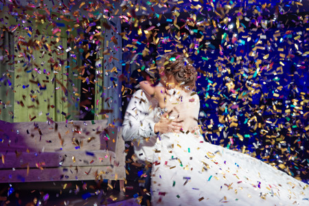 A young couple bride and groom dancing dance in the rain falling multicolored sequins in a darkened room at their wedding.の写真素材