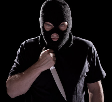 Burglar in mask holding knife on black background
