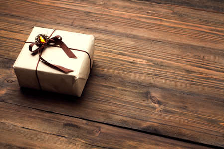 Gift Box on Wood Table, Wrapped Vintage Paper Present With Bow Lying on Brown Wooden Planksの写真素材