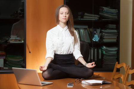 Young beautiful lady in office sitting on the table in yoga poseの写真素材