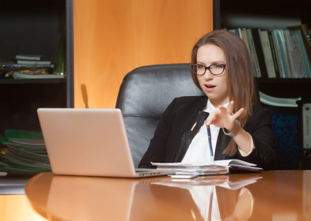 Young beautiful woman sitting on the black leather chair looking into laptop display
