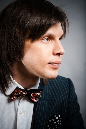 handsome man with long hair brunette and brown eyes in dark suit with stripes and bow tie sitting and looking to right at black backgroundの写真素材