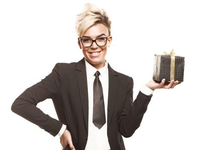 Blond beautiful business lady in white shirt eyeglasses black suit and black tie with gift on white isolated backgroundの写真素材