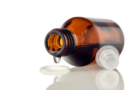 Amber medical bottle with spilled liquid on a white isolated background. Brown glass bottle with liquid close-upの写真素材