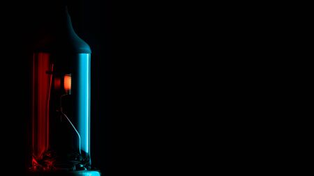 Spare car headlight lamp on black background with red-blue effect.Lighted car light bulb in the dark with place for text.の写真素材