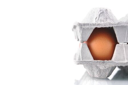 Chicken eggs in a cardboard box on a white isolated background. Brown organic chicken eggs on a white specular surface, closeup.の写真素材