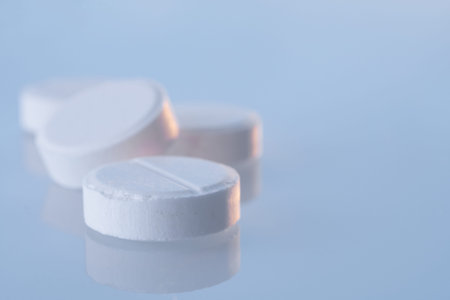 White round pills on a blue mirror surface with copy space, closeup. Medicines on glass lit by the...