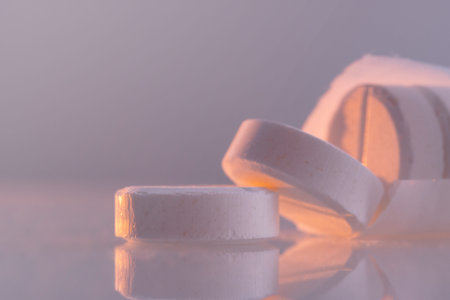 White round pills on a mirror surface, close-up. Medicines on glass lit by the morning sun.