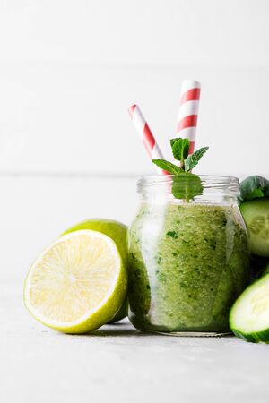 Jars with green smoothie and red tubules on a light background. Freshly made vegetable smoothie. Close up. Glass jars with green smoothie on a concrete background.の写真素材