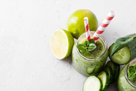 Jars with green smoothie and red tubules on a light background. Freshly made vegetable smoothie. Close up. Glass jars with green smoothie on a concrete background.の写真素材